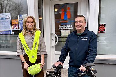 Eine Frau mit Warnweste und ein Mann mit Herrenrad stehen vor einem Ladeneingang.