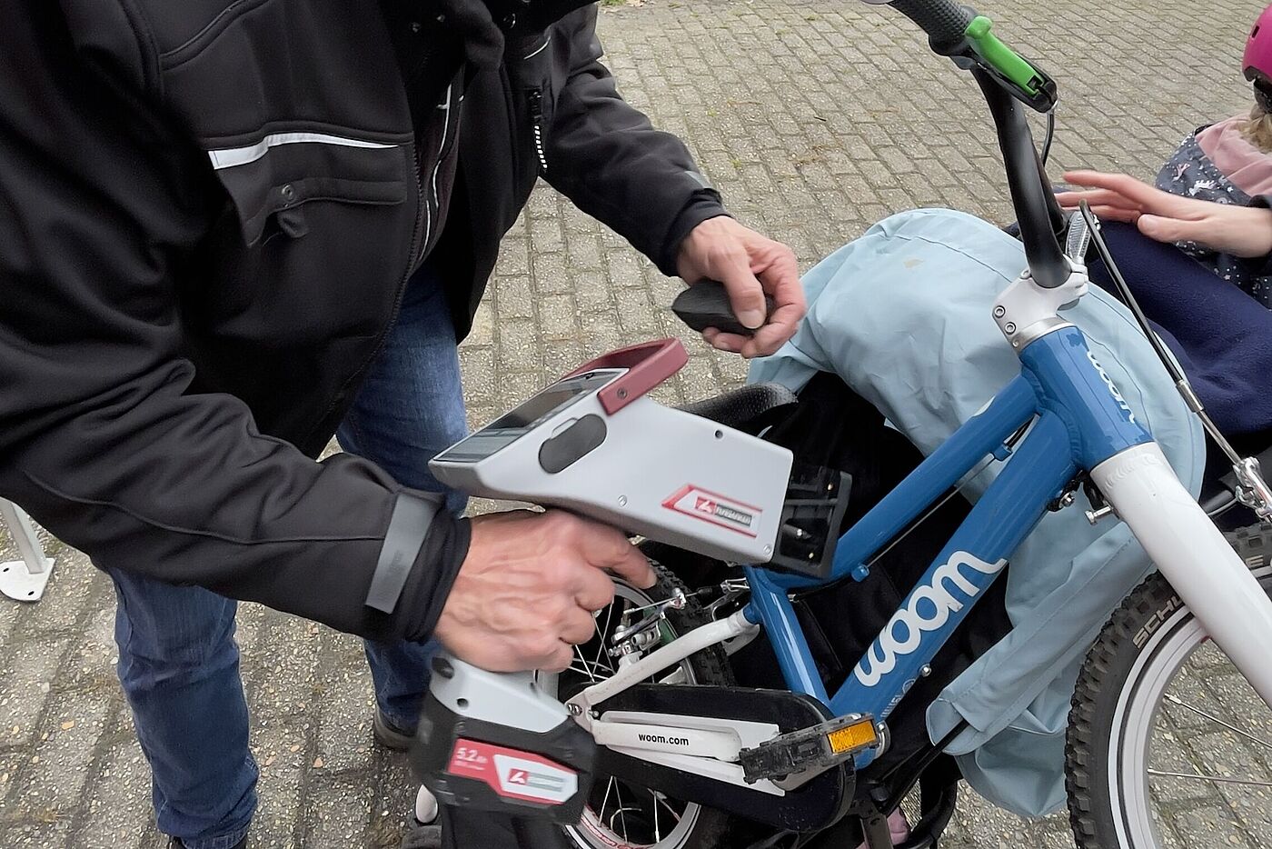 Ein Mann mit Schirmmütze hält ein graues Codier-Gerät in der Hand. Er codiert damit ein blau-weißes Kinderfahrrad.